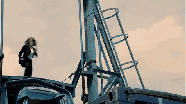 a woman is standing on top of a blue structure with a ladder leading up to it