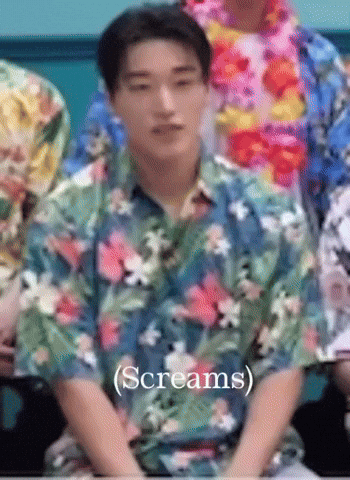 a man wearing a hawaiian shirt is sitting in front of a group of people and screaming .