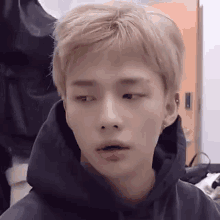 Hyunjin gives a tired sideways look while seated indoors.