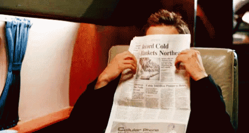 A person hides their face behind a newspaper while seated in a chair.