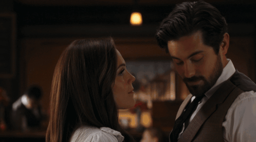 A formally dressed couple talks closely in a dim restaurant-like room.