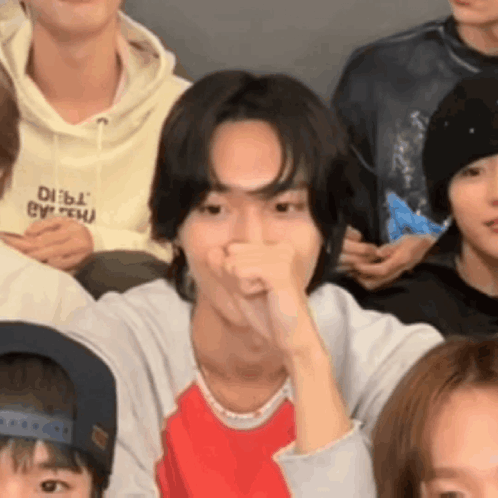 a group of young people are sitting in a room and one of them is covering his mouth with his hand .