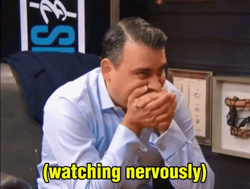 A man covers his mouth and watches nervously in a studio setting.