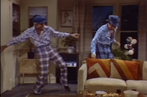 two men are dancing in a living room with a couch