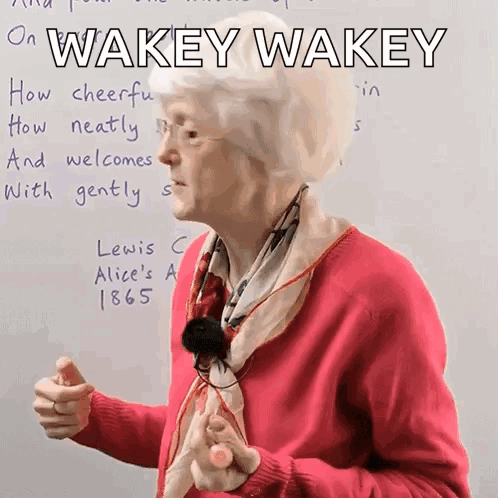 An older woman points at a board reading “WAKEY WAKEY,” encouraging people to get moving.