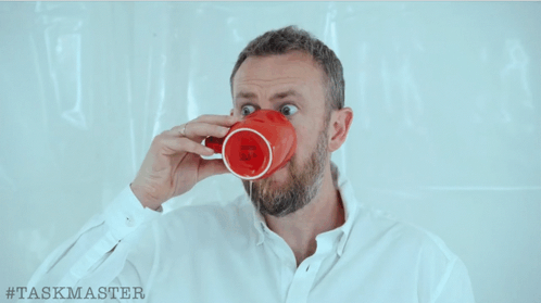 a man drinking from a red mug with # taskmaster written on the bottom