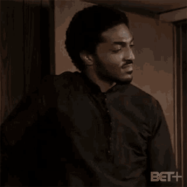 a man in a black shirt and tie is standing in front of a door and says okay .