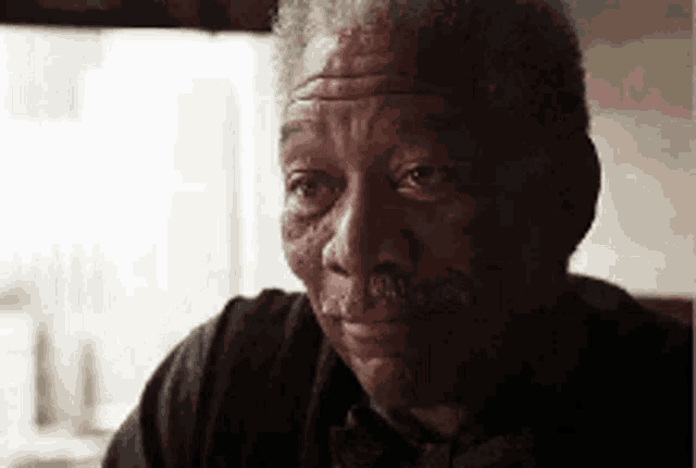 Morgan Freeman gives a serious, knowing look in a dimly lit close-up.