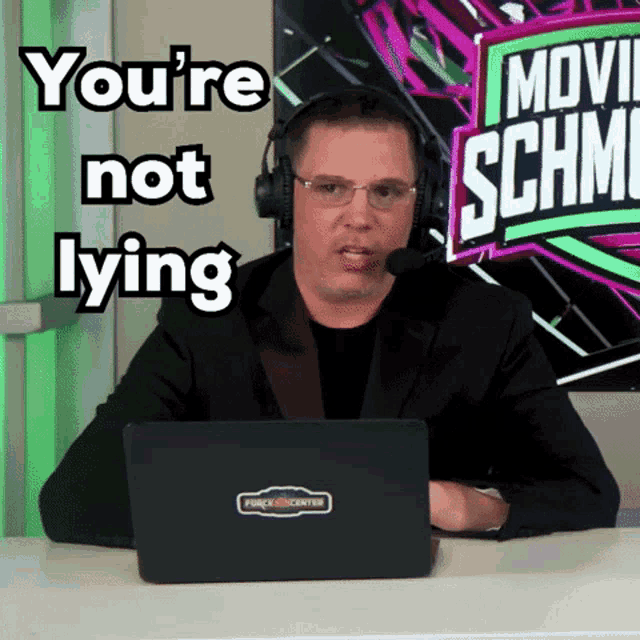 a man wearing headphones and glasses is sitting in front of a sign that says " you 're not lying "