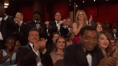 A large audience claps enthusiastically in a theater.