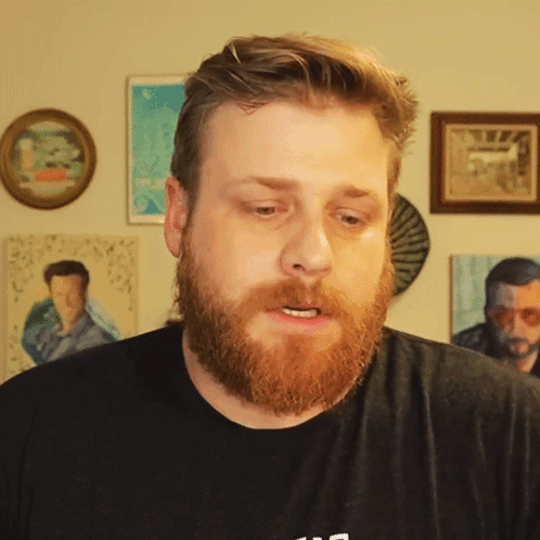 a man with a beard wears a black shirt with the letter s on the front