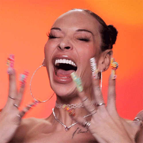 A drag performer throws both hands up and screams with excitement against an orange backdrop.