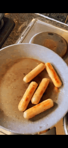 sausages are being cooked in a frying pan on a stove .
