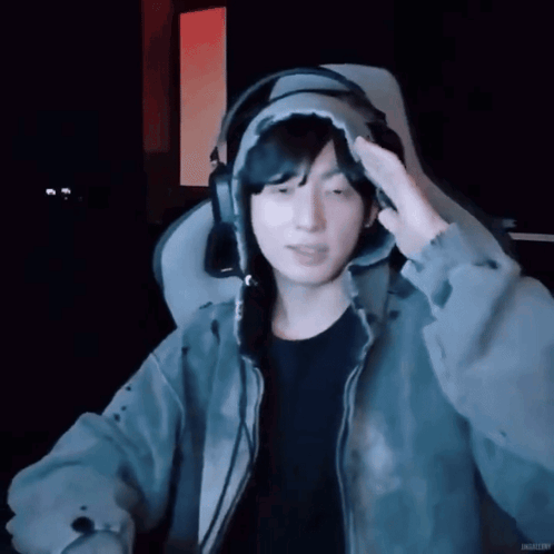 A streamer wearing headphones lifts a hand to his head.