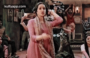 a woman in a pink dress is dancing with a tambourine in a room .