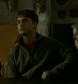 a man wearing glasses is sitting in a dark room with his hand in the air