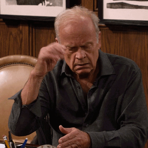 Dr. Frasier Crane rests his temple on his hand, looking troubled.