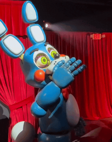a toy bunny is standing in front of a red curtain with an exit sign in the background