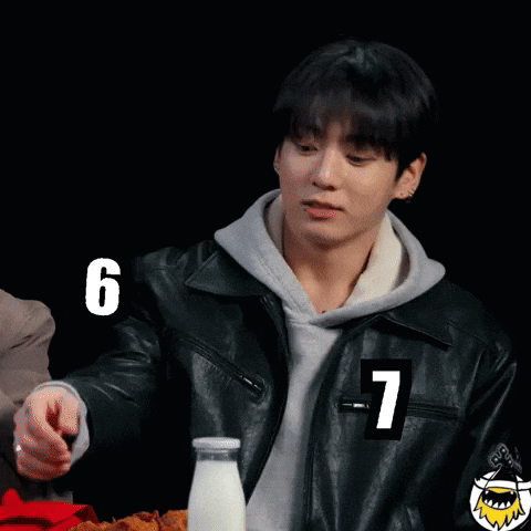 A man in a leather jacket sits at a table beside large “6” and “7” graphics.