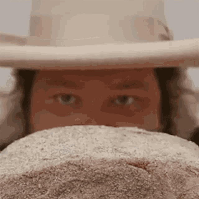 a man wearing a cowboy hat is covering his face with a large rock .