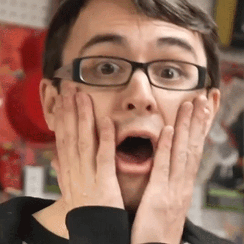 A glasses-wearing man presses both hands to his cheeks with his mouth open.