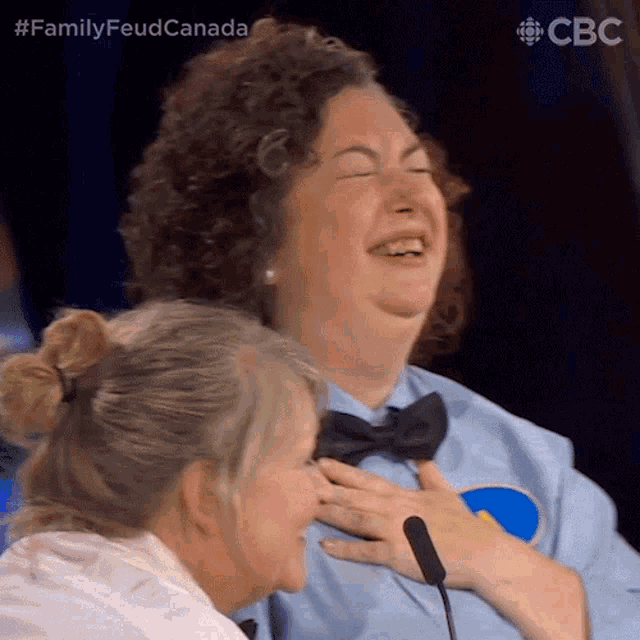 a woman is laughing while another woman holds her hand to her chest .