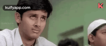 a man is making a funny face while sitting in a classroom with other students .