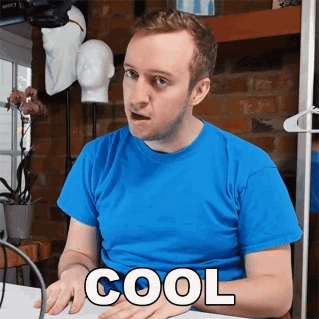 a man in a blue shirt is sitting at a desk with the word cool written on his shirt