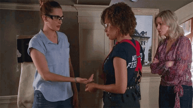 a woman wearing a shirt that says " mighty fire " talks to two other women