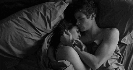 A couple cuddles closely together in bed in a dark scene.