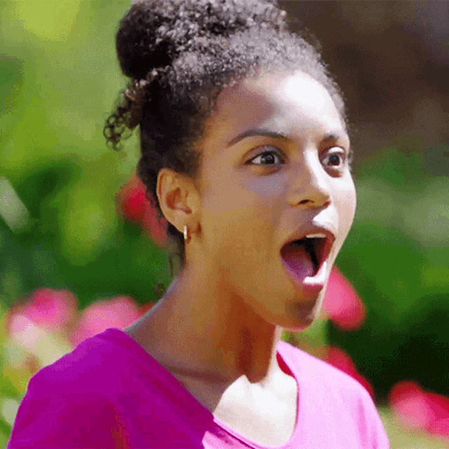 a woman in a pink shirt is making a surprised face with her mouth open