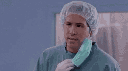 A man in surgical scrubs looks baffled in a clinical room.