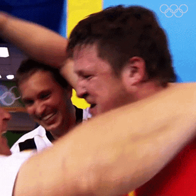 two men are hugging in front of a sign that says olympic rings