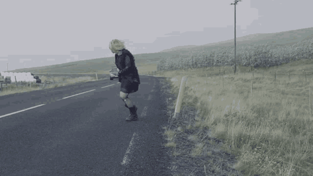 a woman standing on the side of a road with a car in the background
