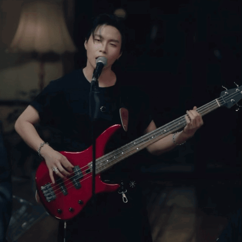 a man singing into a microphone while playing a red bass guitar