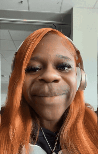 a woman with orange hair wearing headphones making a funny face