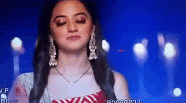 a woman wearing a necklace and earrings is standing in front of a blue background with candles .