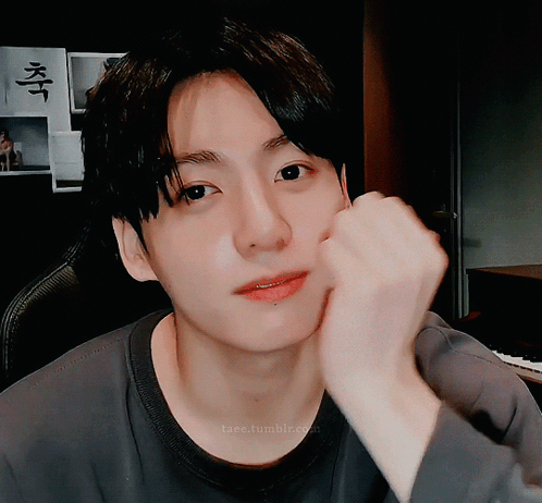 A man rests his cheek on his fist and looks sweetly at the camera.
