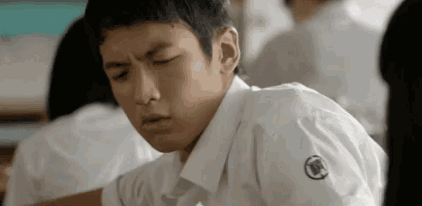 a young boy in a school uniform is sitting at a desk in a classroom .