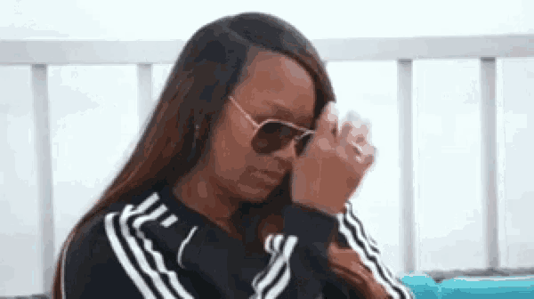 a woman wearing sunglasses and a black and white adidas jacket is sitting on a couch .