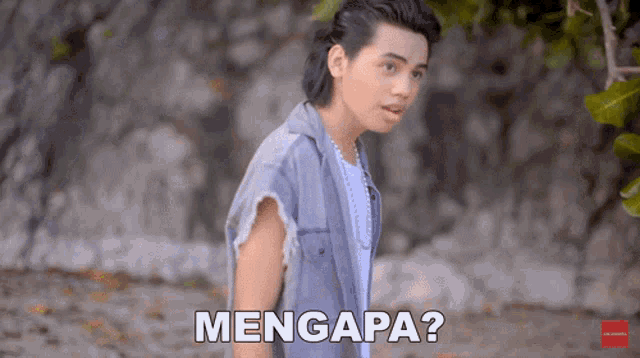 a young man standing in front of a wall with the words mengapa written below him