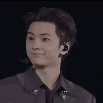 a young man wearing a black jacket and earphones is smiling and talking to someone .