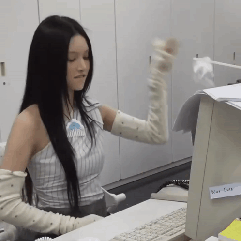 a woman wearing gloves is sitting at a desk in front of a computer with a note that says not a question on it