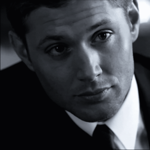 Dean Winchester gives a knowing wink in a black-and-white close-up.