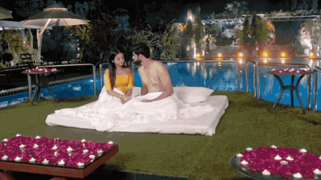 a man and woman are laying on a bed near a pool