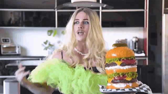 a woman in a green dress is holding a giant hamburger on a checkered napkin