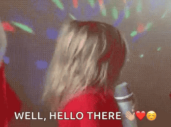 A performer flips their hair while holding a microphone, captioned “WELL, HELLO THERE.”