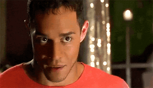 a man in a red shirt looks at the camera with a surprised look on his face