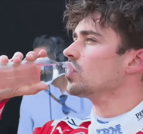 a man is drinking water from a bottle while wearing a red shirt with ibm on it .