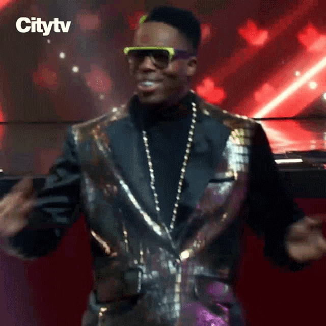 a man in a sequined jacket and sunglasses is dancing on a stage with the citytv logo behind him